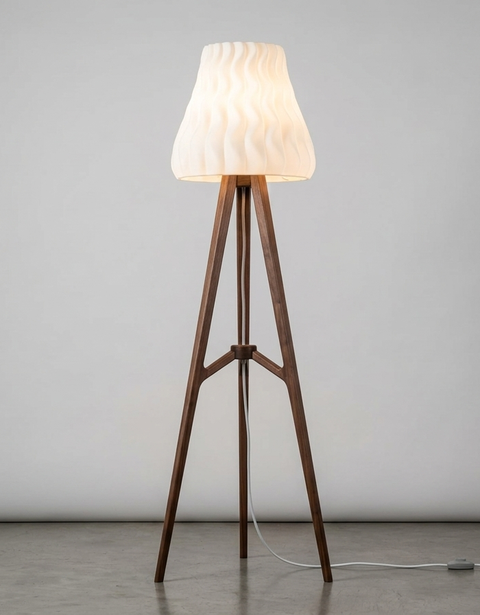 A 3D printed tripod floor lamp lit against a plain studio wall